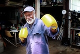 Older man holding up yellow boxing gloves.