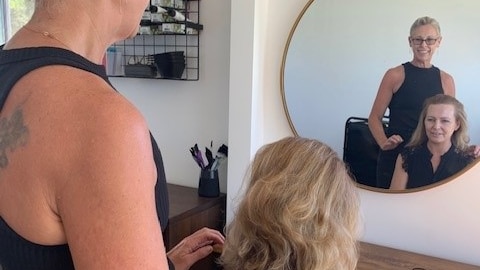 A woman stands behind another woman in front of a mirror.