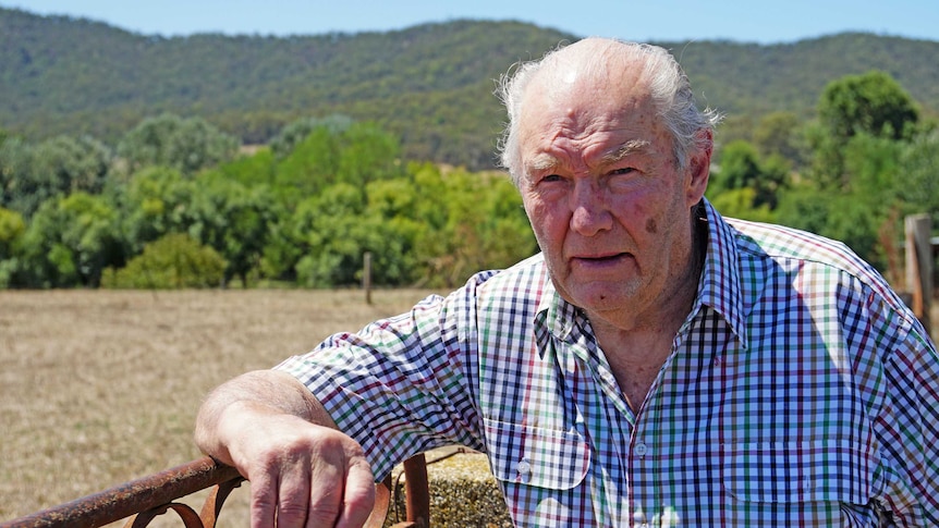 David White leans on a gate with a field and mountains behind him.