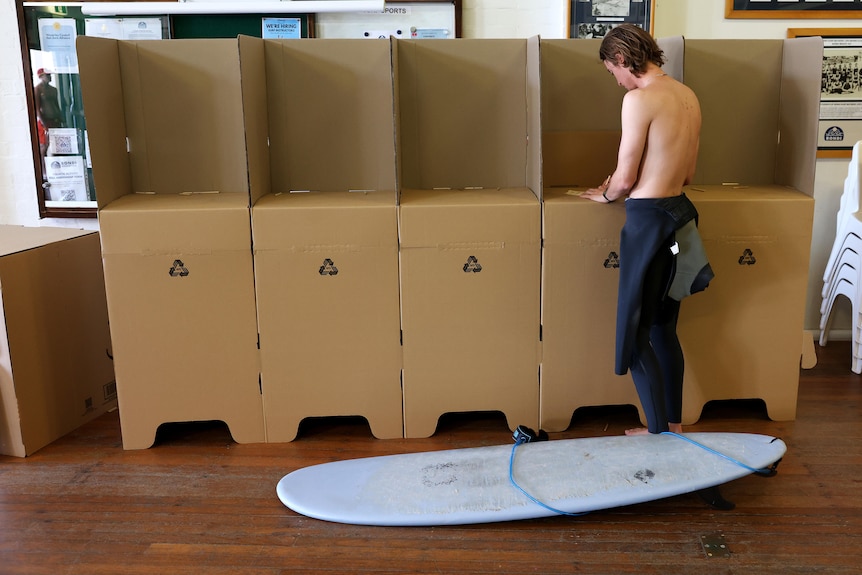 a surfer with his surfboard on the floor votes at a polling centre in  bondi for the indigenous voice to parliament referendum