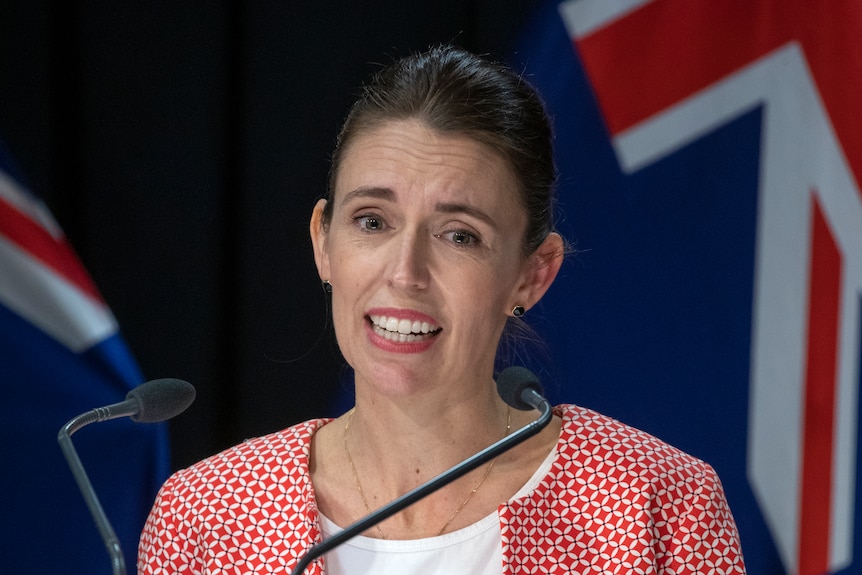 Jacinda Ardern stands in front of New Zealand flags with a worried look on her face