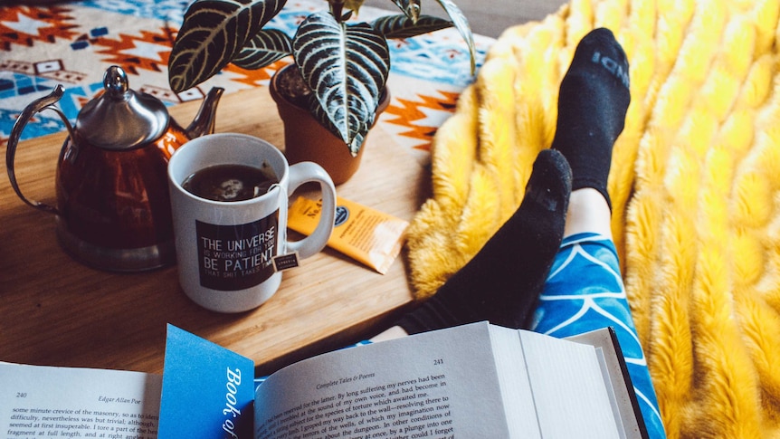 Person drinking tea, reading a book and wearing comfy socks.