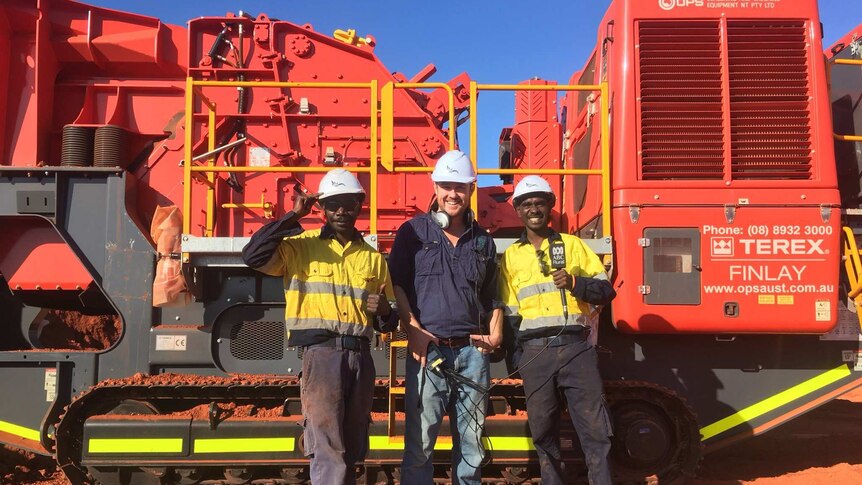 three men standing in front of mining equipment.