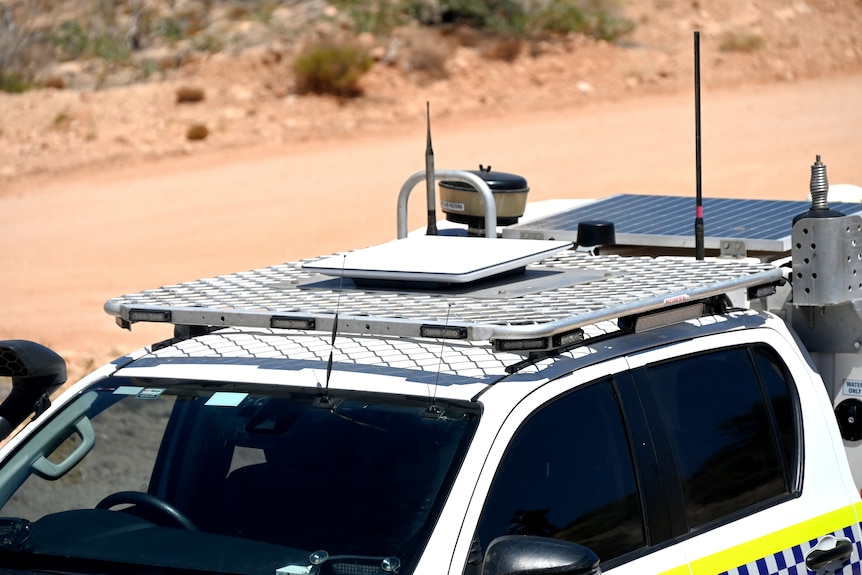 A white four-wheel-drive police car close-up with a white square in the middle of a silver roof rack.