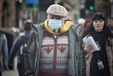 A man in a mask and warm clothing walks down a busy CBD street.