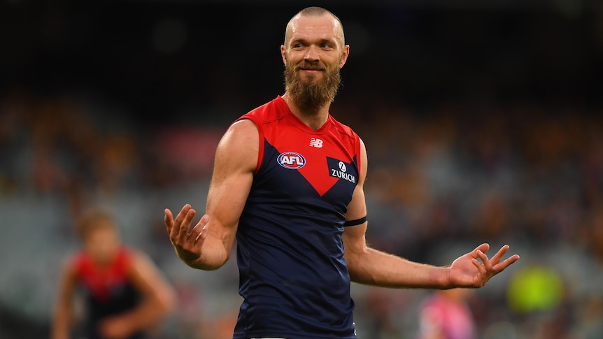 A Melbourne Demons AFL player smiles as he stands with his arms held out to his sides after kicking a goal.