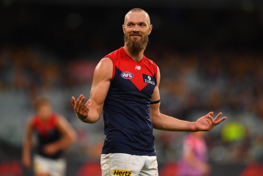 A Melbourne Demons AFL player smiles as he stands with his arms held out to his sides after kicking a goal.