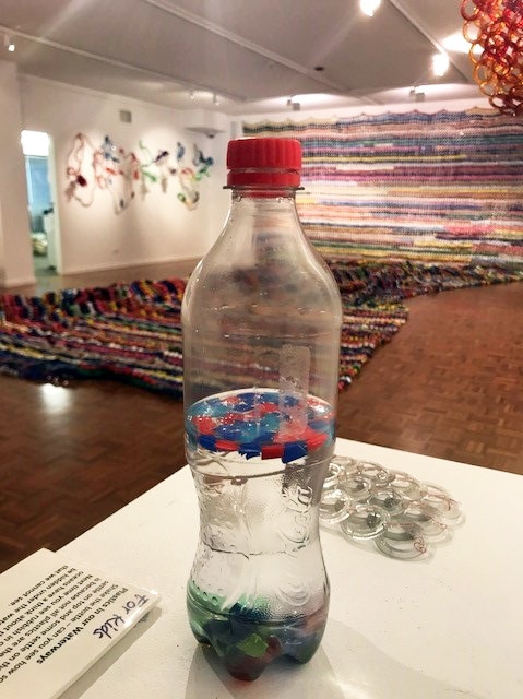 A clear plastic bottle half filled with water has some pieces of plastic floating and some which have sunk to the bottom.