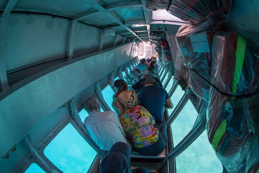 A group of tourists sit looking out the windows of a semi-submersible.