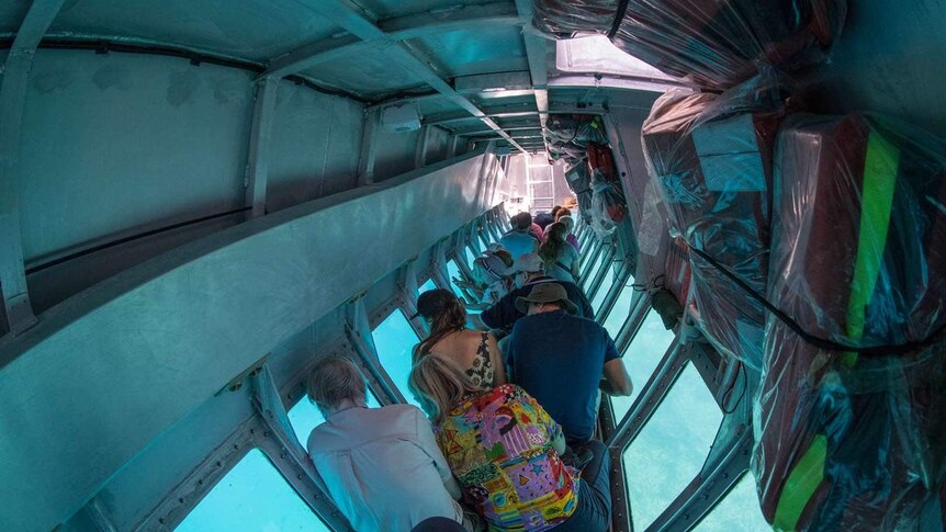 A group of tourists sit looking out the windows of a semi-submersible