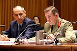 Major-General Andrew Bottrell, in uniform, sits behind a desk speaking into microphones.