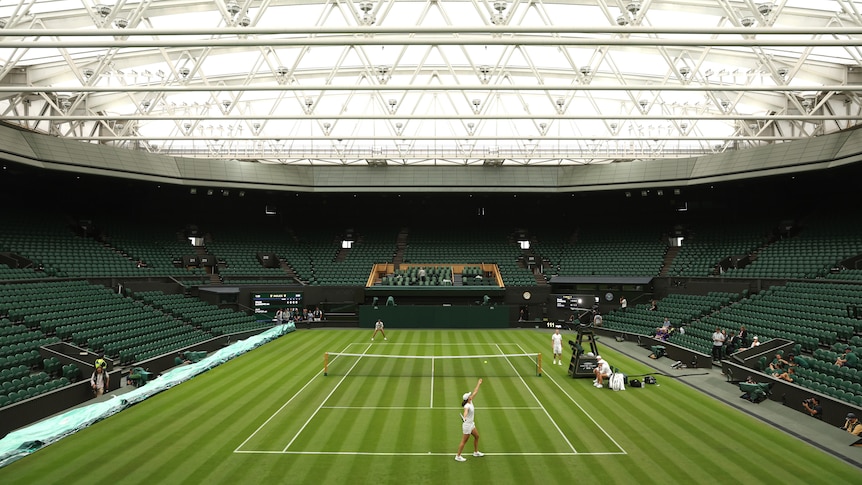 A wide shot looking down the main Centre Court at Wimbledon towards the scoreboard, while players dressed in all-white train.