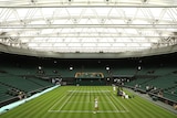 A wide shot looking down the main Centre Court at Wimbledon towards the scoreboard, while players dressed in all-white train.