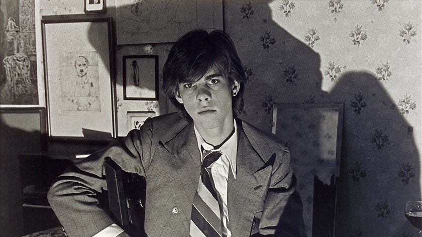 Black and white photo of a young man in a wide tie with shadows on the wall behind him.