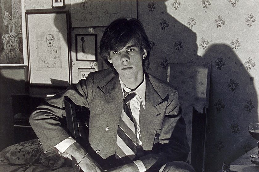 Black and white photo of a young man in a wide tie with shadows on the wall behind him.