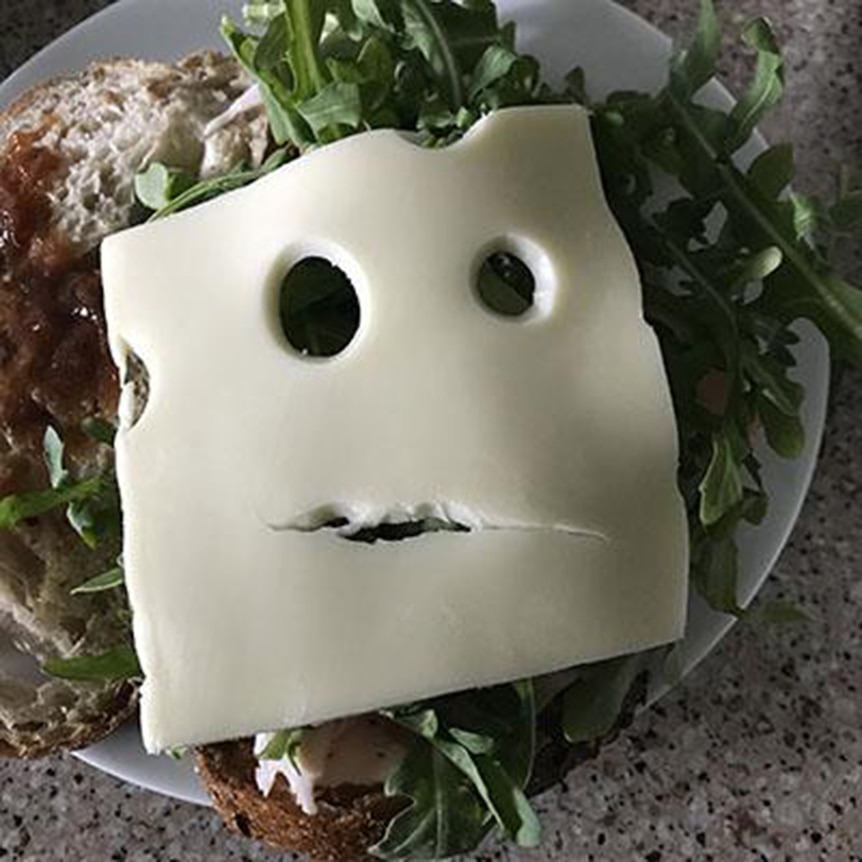 An open sandwich topped with a slice of Swiss cheese that has holes in the pattern of a face. 