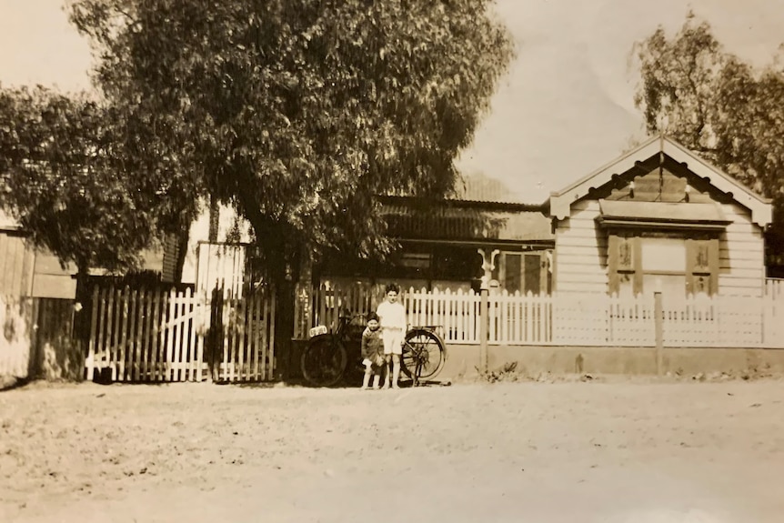 Two young boys stand in front of a family home taken on a very old camera.