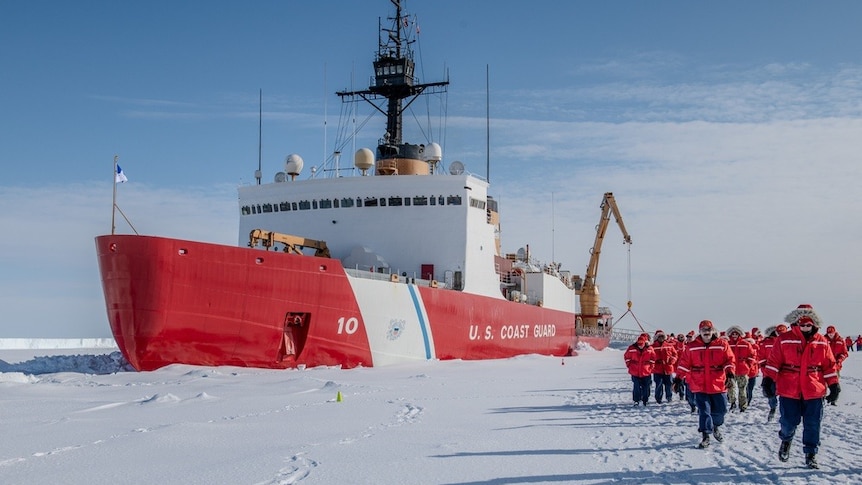 A red ship in sea ice with crew walking around.