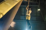 A protester scales down a rope hanging from the side of a bridge with a dim green light lighting him up at night.
