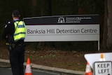 A sign outside Banksia Hill Detention Centre with a police officer nearby.
