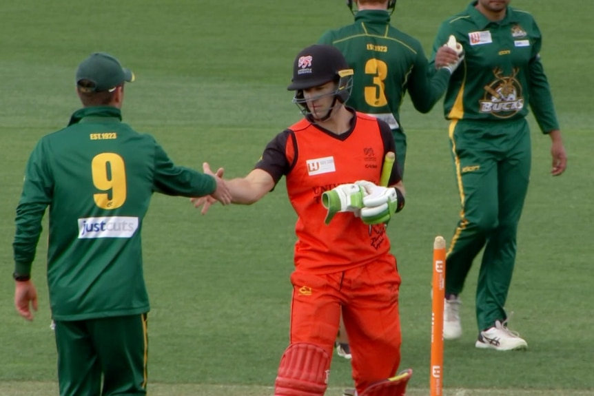 A cricket player in red shakes the hand of another cricket player in green