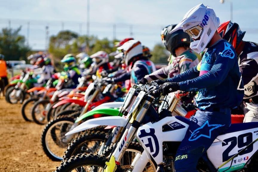 Motocross riders on their bikes at the starting line for a race.  