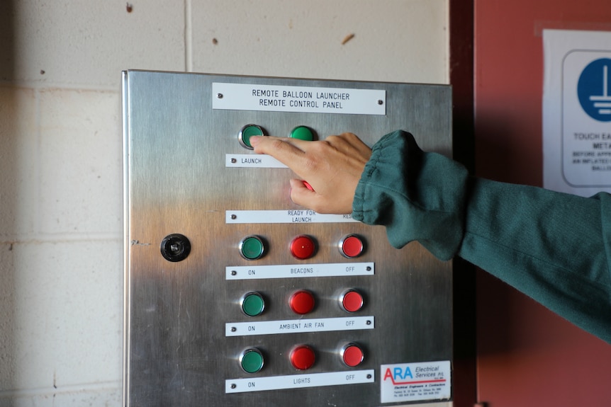 An observer pushes a button on a control panel for launching weather balloons remotely.