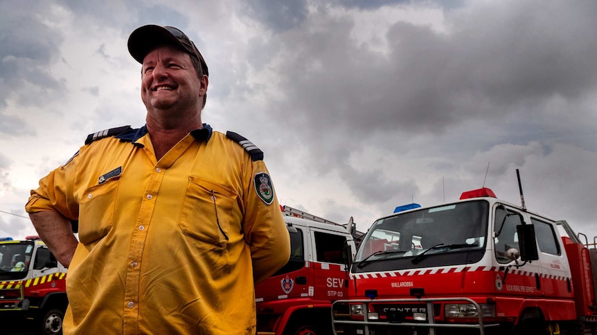 A man in front of fire engines with a stormy sky in the background