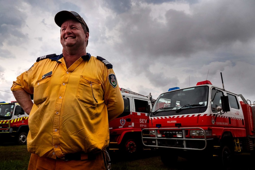 A man in front of fire engines with a stormy sky in the background