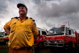 A man in front of fire engines with a stormy sky in the background