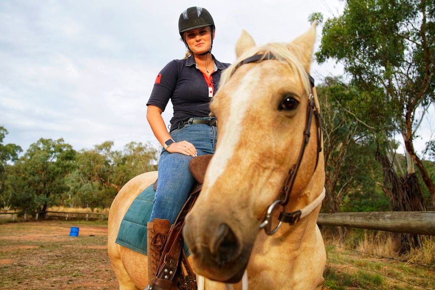 A girl with blonde hair smiles while riding a horse.