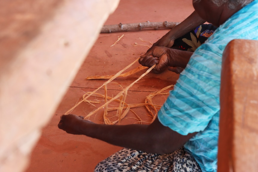 A Burarra woman sits pulling apart a string-like bark called Burdaga.