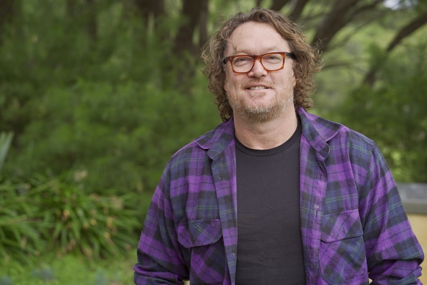 Man wearing purple and black check shirt and glasses