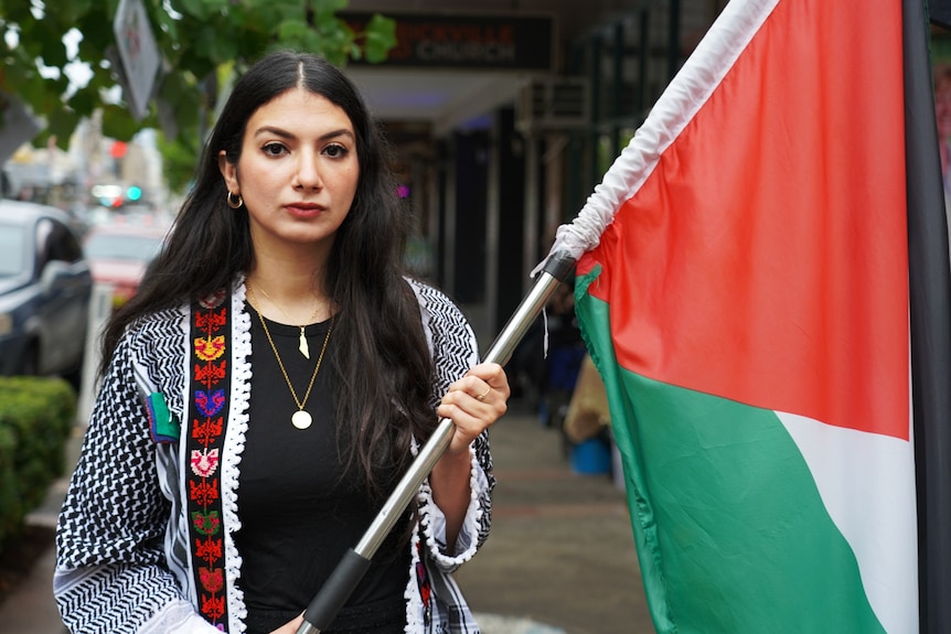 A woman holding a Palestinian flag stares at the camera.
