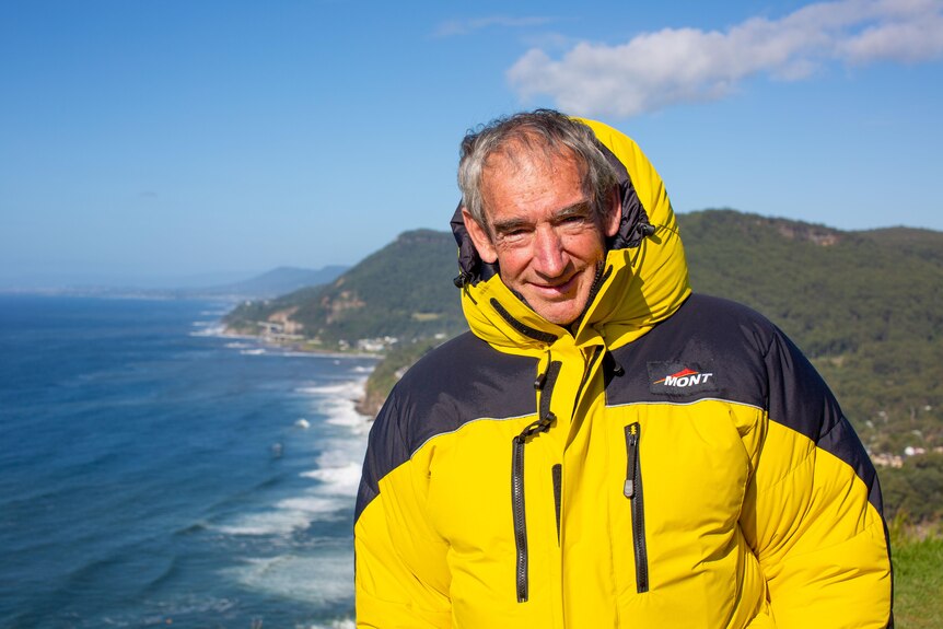 Ken Hutt wearing a yellow jacket standing high over a coastline.