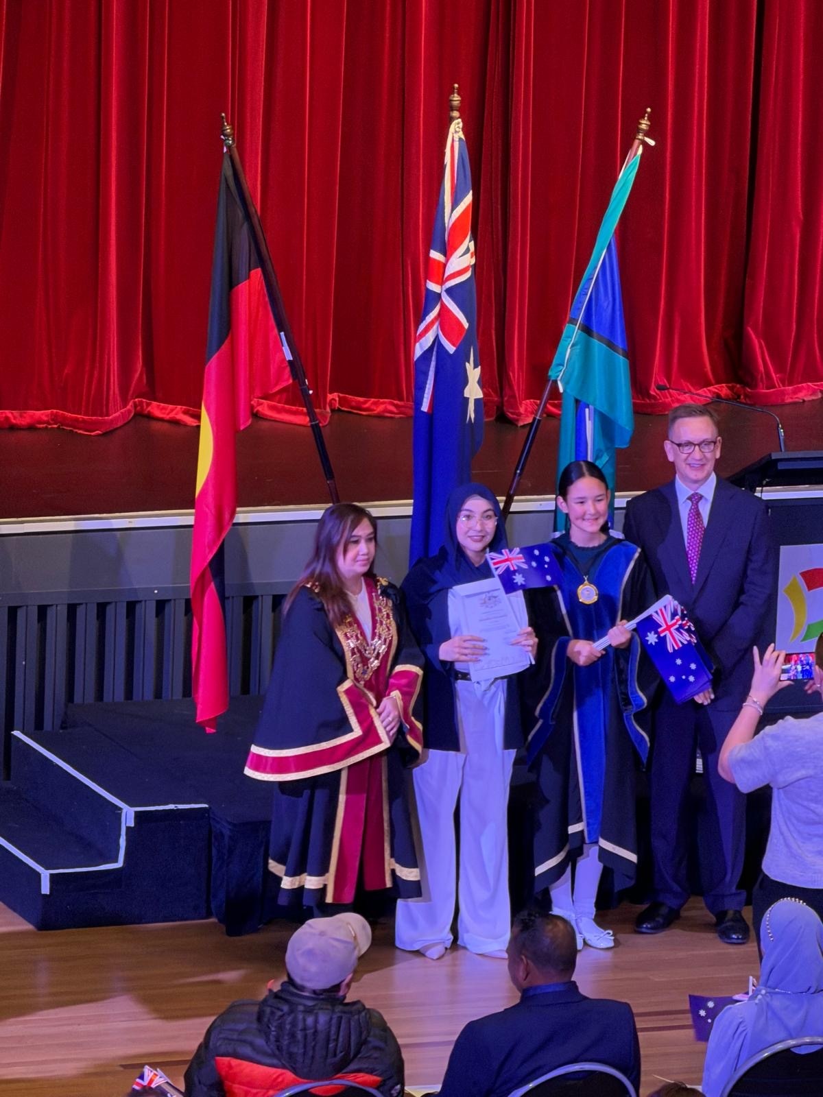 A group of people smile in front of Australian, Aboriginal and Torres Strait Island flags at a citizenship ceremony