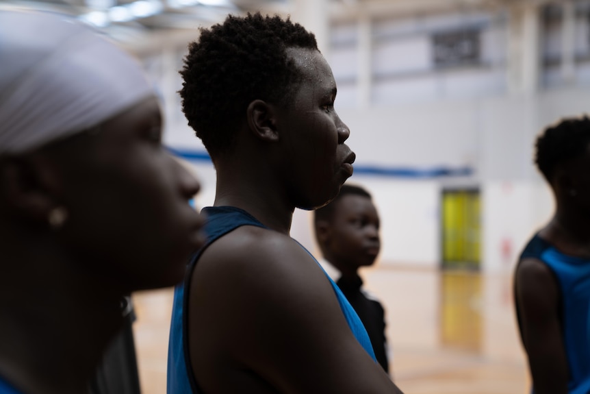 An African teenage boy standing on the side of a basketball court