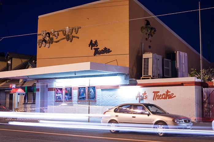 Exterior photo of the Brisbane Arts Theatre at night with bright street lights, lighting up the brick building and parked cars