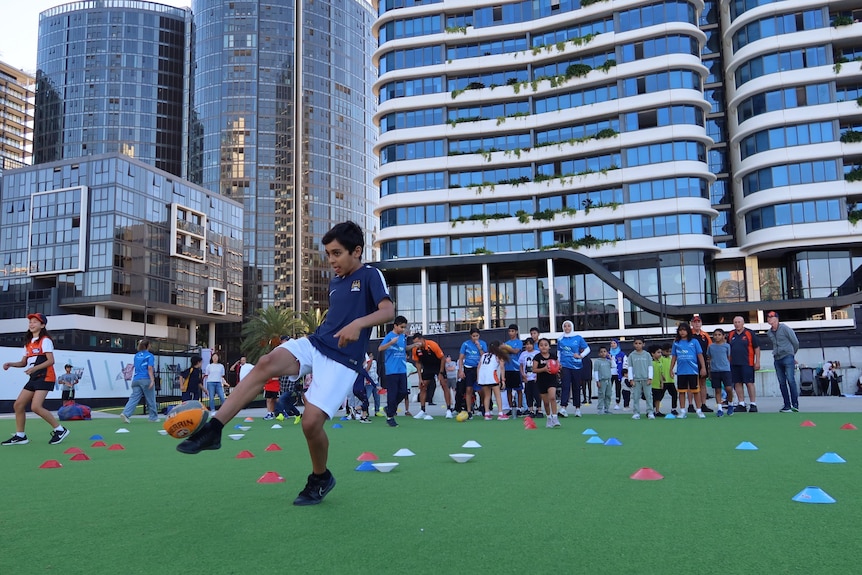 A boy kicks an AFL ball, with a huge building in the background