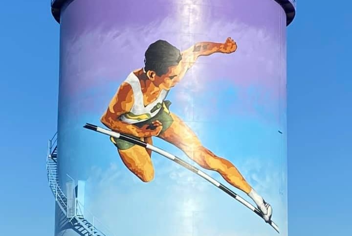 A man leaping over a high jump bar, painted on the side of a silo.