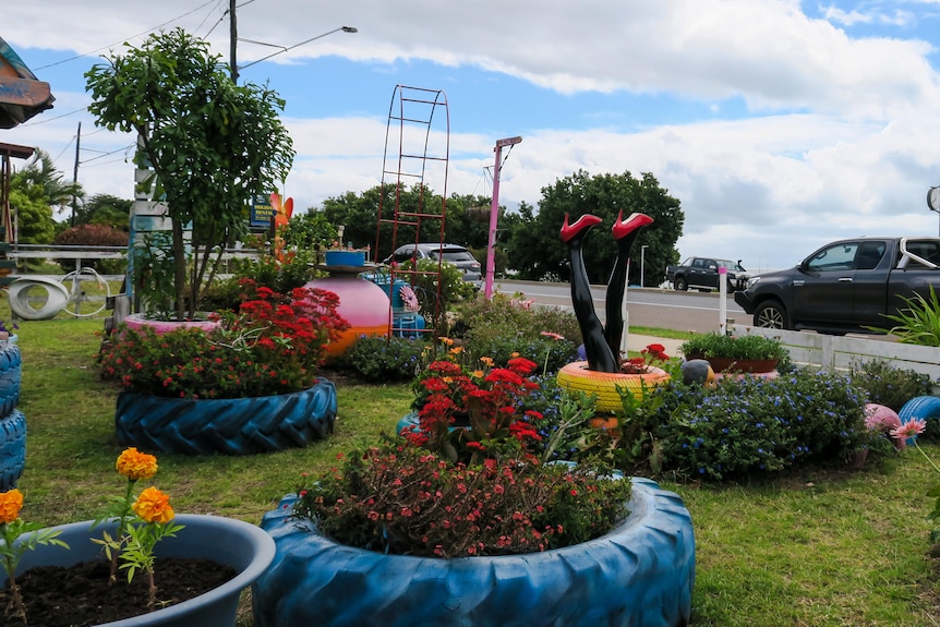 Facing the road from the garden, garden beds filled with flowers and succulents, a mannequin pair of legs stick out of one