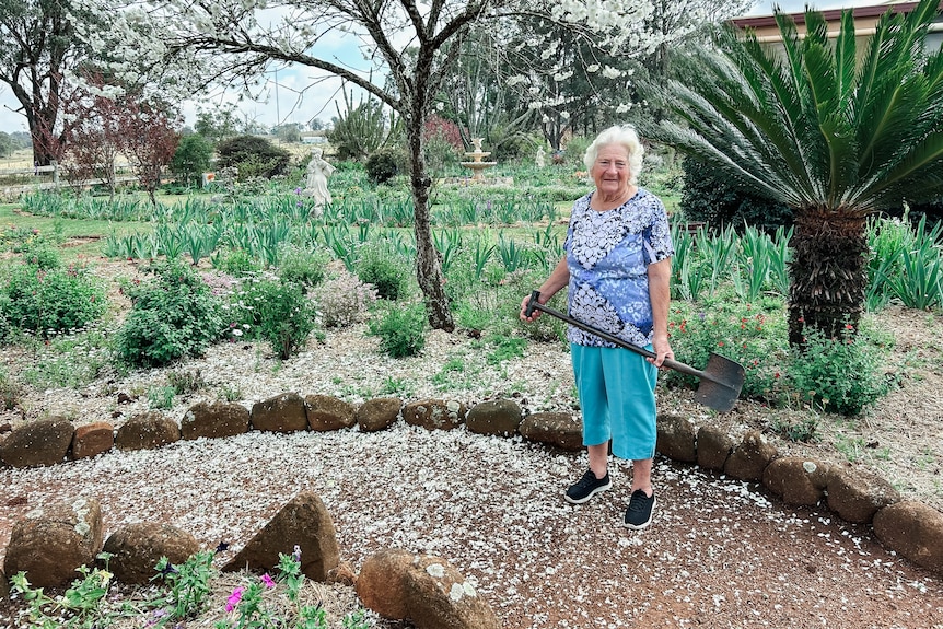 a woman holding a spade stands in front of a garden bed