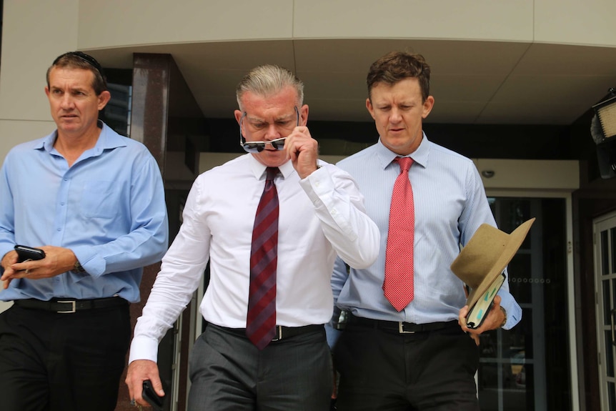 Jon Tippett puts on sunglasses while walking with two other people out of Darwin Supreme Court.