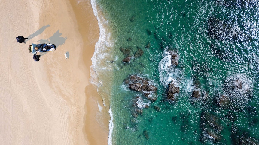 Aerial shot of a person sitting on a stretcher on a sandy beach.