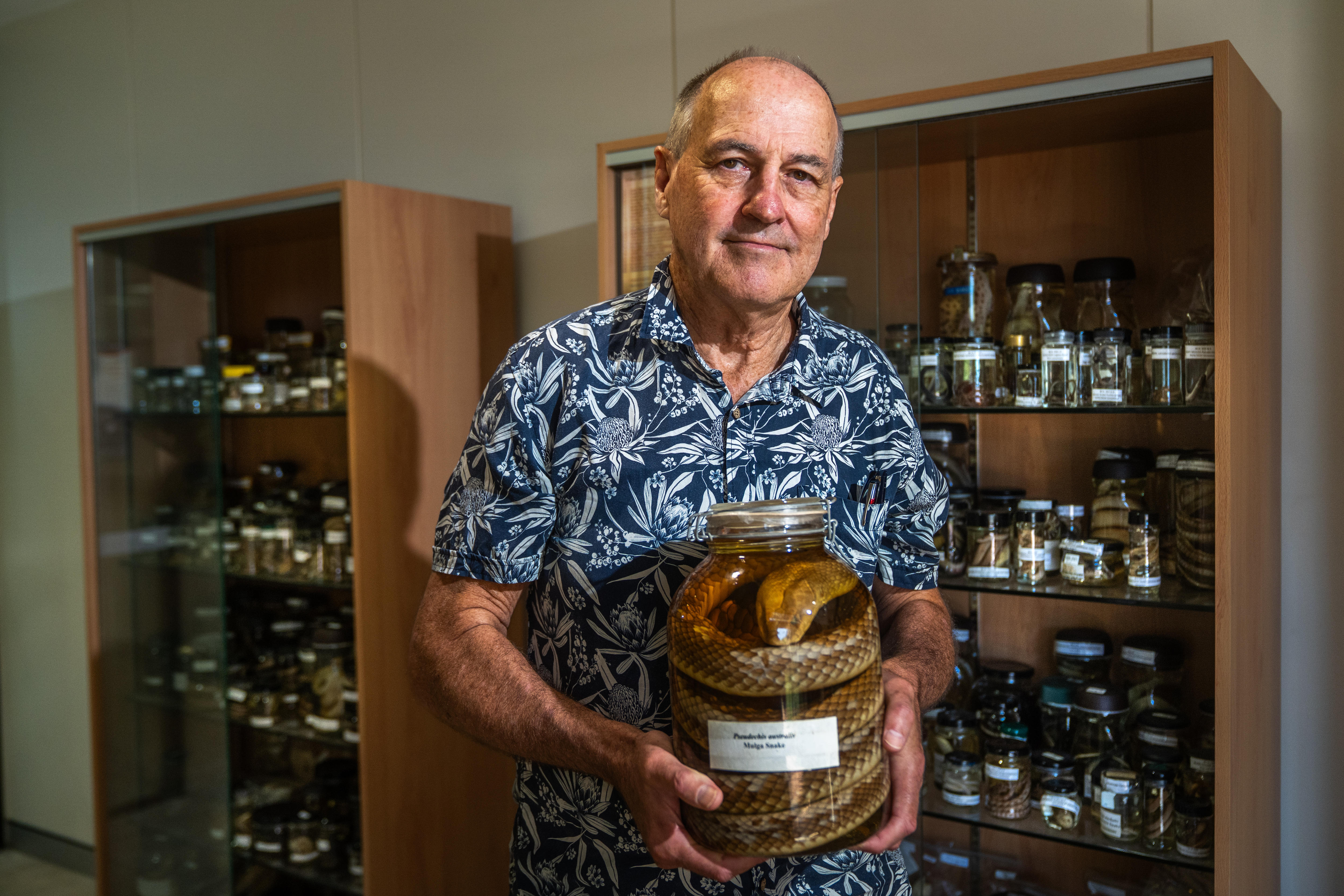 A man holds a snake suspended in a specimen jar