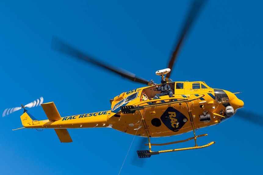 A rescue helicopter hovers in a clear sky.
