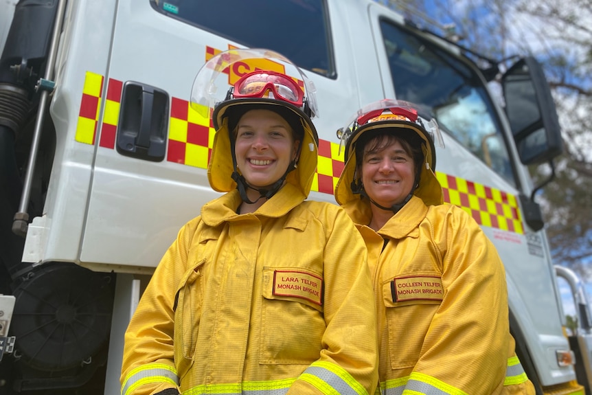 Two women standing in front of a truck wearing protective gear.