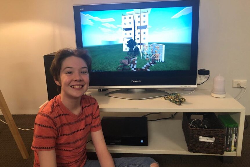A teenage boy sits on the floor in front of a television screen. 