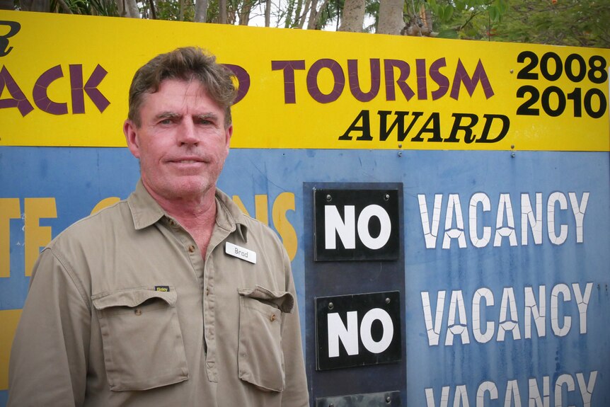 A man stands in front of a sign displaying no vacancy at a holiday park. 
