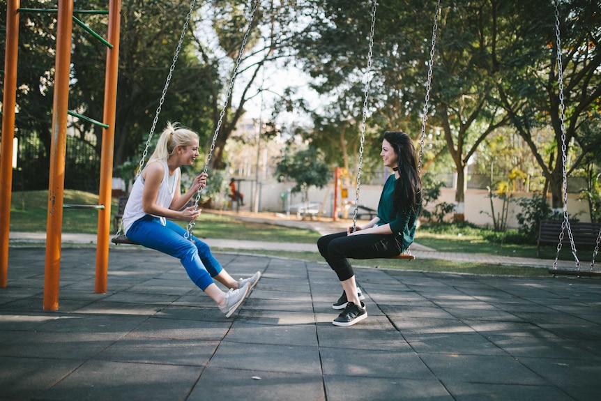 Two women sit on swings talking and smiling
